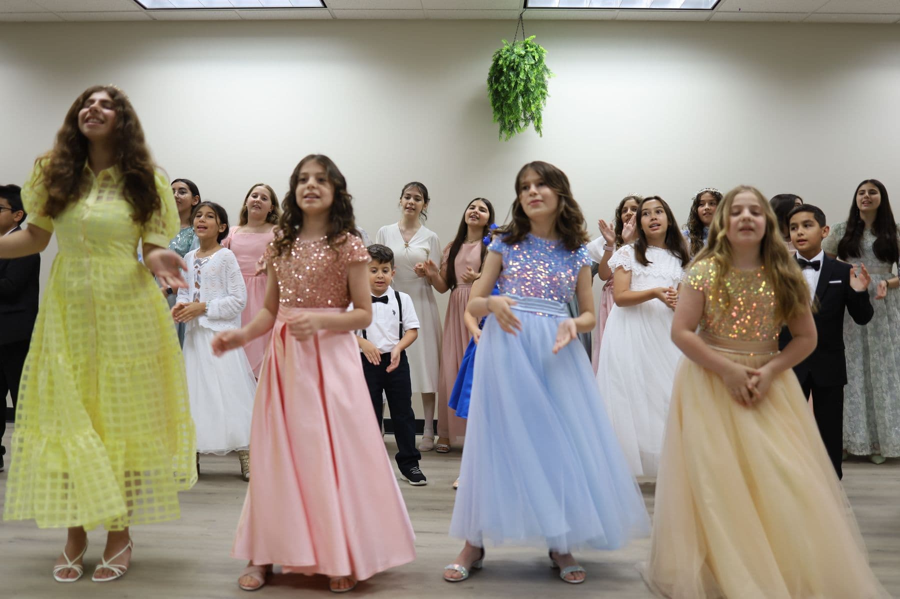 Dozens of children in festive dresses rehearse together